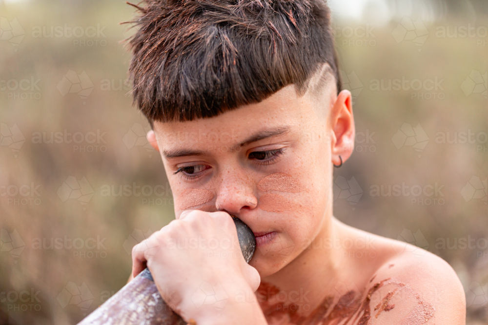 aboriginal child playing didgeridoo wearing traditional ochre body paint - Australian Stock Image