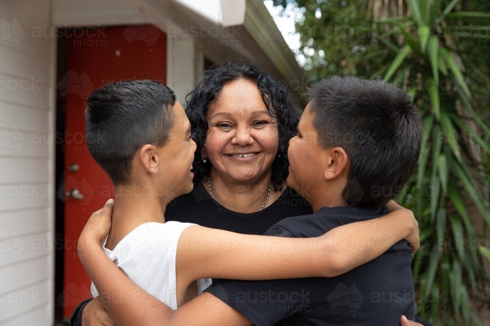 Aboriginal family hugging and kissing in backyard - Australian Stock Image