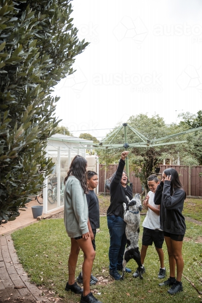 Aboriginal family playing with dog in backyard - Australian Stock Image