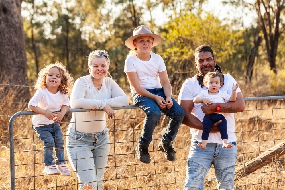 Aboriginal family portrait on farm paddock gate with parents and children - Australian Stock Image