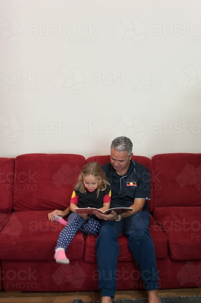 Aboriginal father and daughter reading on lounge - Australian Stock Image