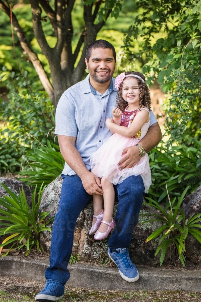 Aboriginal father sitting with daughter on lap smiling - Australian Stock Image