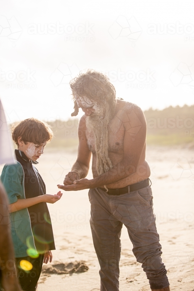Aboriginal father with body paint helping his son on a beach - Australian Stock Image
