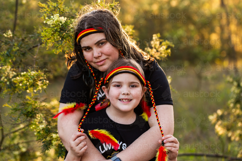 Aboriginal girl and big sister with red yellow and black headband in Australian bushland - Australian Stock Image