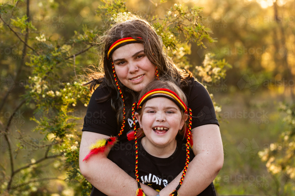 Aboriginal girl and big sister with red yellow and black headband in Australian bushland - Australian Stock Image