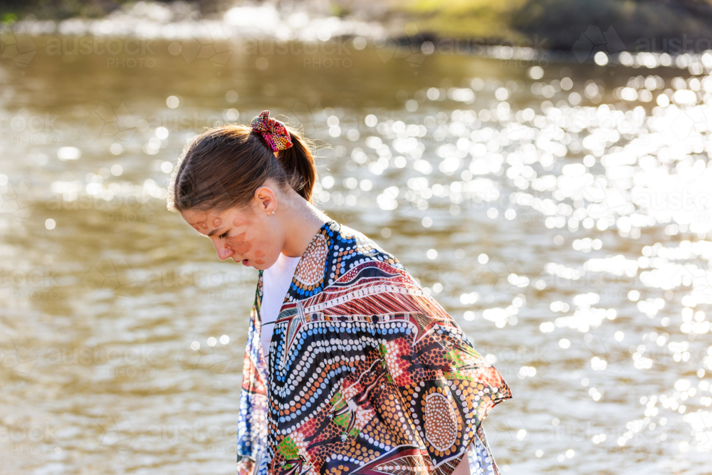 Aboriginal girl looking down by water of Hunter River (The Coquun) on sunny morning - Australian Stock Image