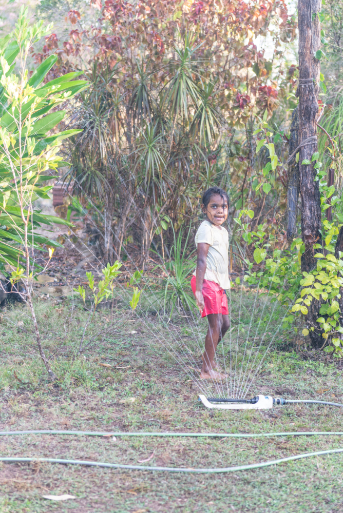 Aboriginal girl playing with sprinklers in backyard - Australian Stock Image