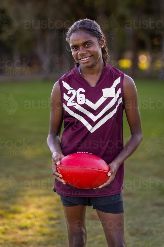 aboriginal girl smiling and holding a red leather football - Australian Stock Image