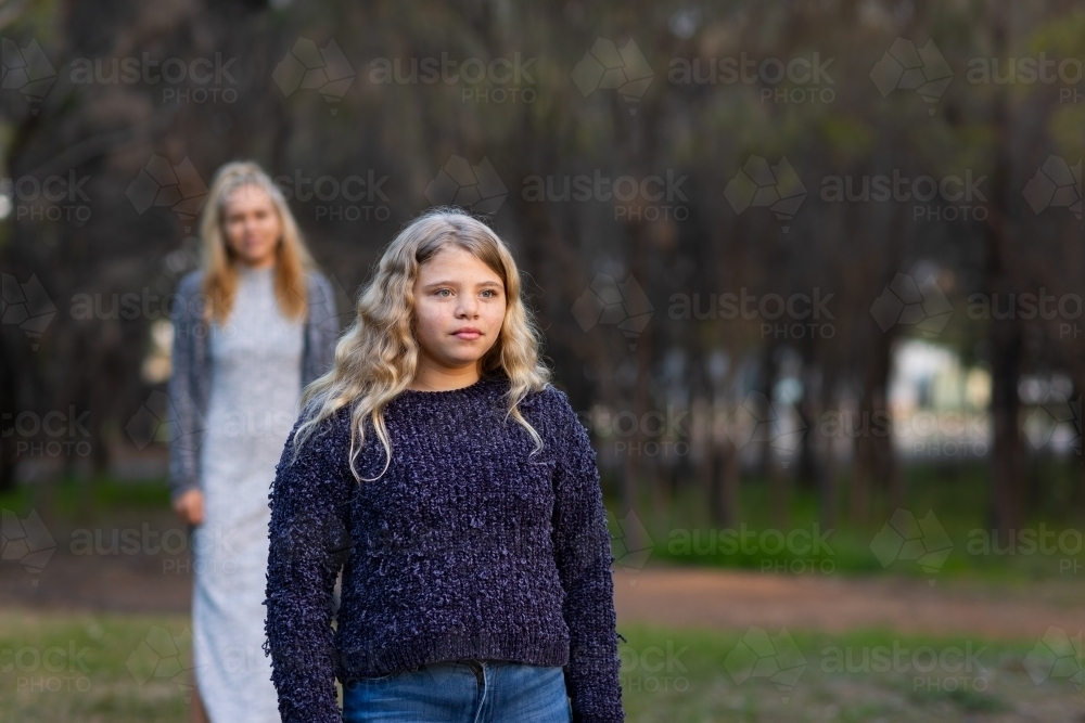 aboriginal girl with long blonde looking into distance with her mum blurred in the background - Australian Stock Image