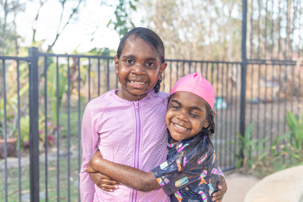 Aboriginal girls by the pool fence hugging - Australian Stock Image