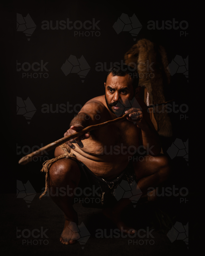 Aboriginal male crouching down aiming spear - Australian Stock Image