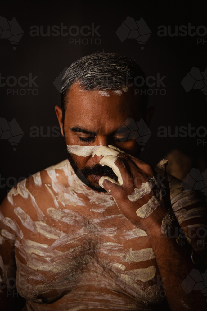 Aboriginal male painting up face with ochre headshot - Australian Stock Image