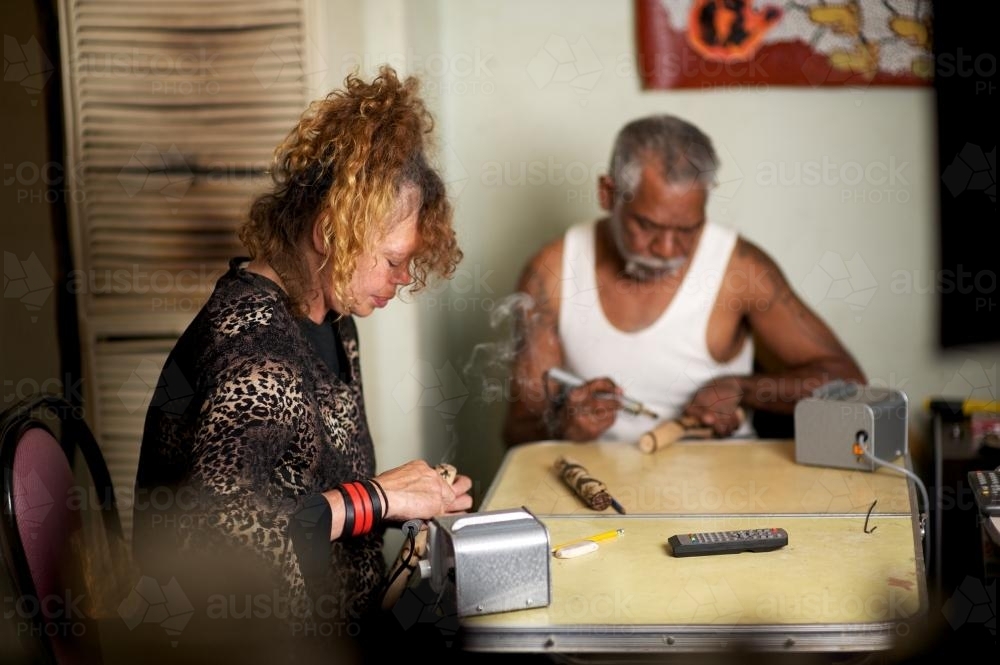 Aboriginal Man and Woman use Wood Burners for Making Message Sticks - Australian Stock Image