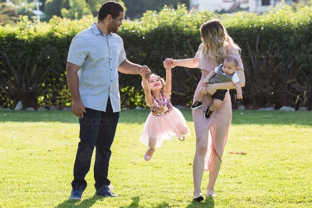 Aboriginal man Caucasian woman with children swinging daughter - Australian Stock Image