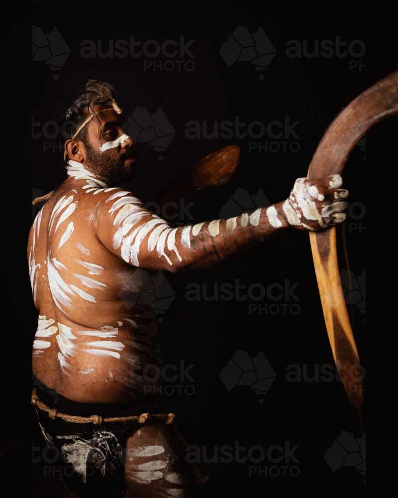 Aboriginal man holding a pair of boomerangs in a dark background. - Australian Stock Image