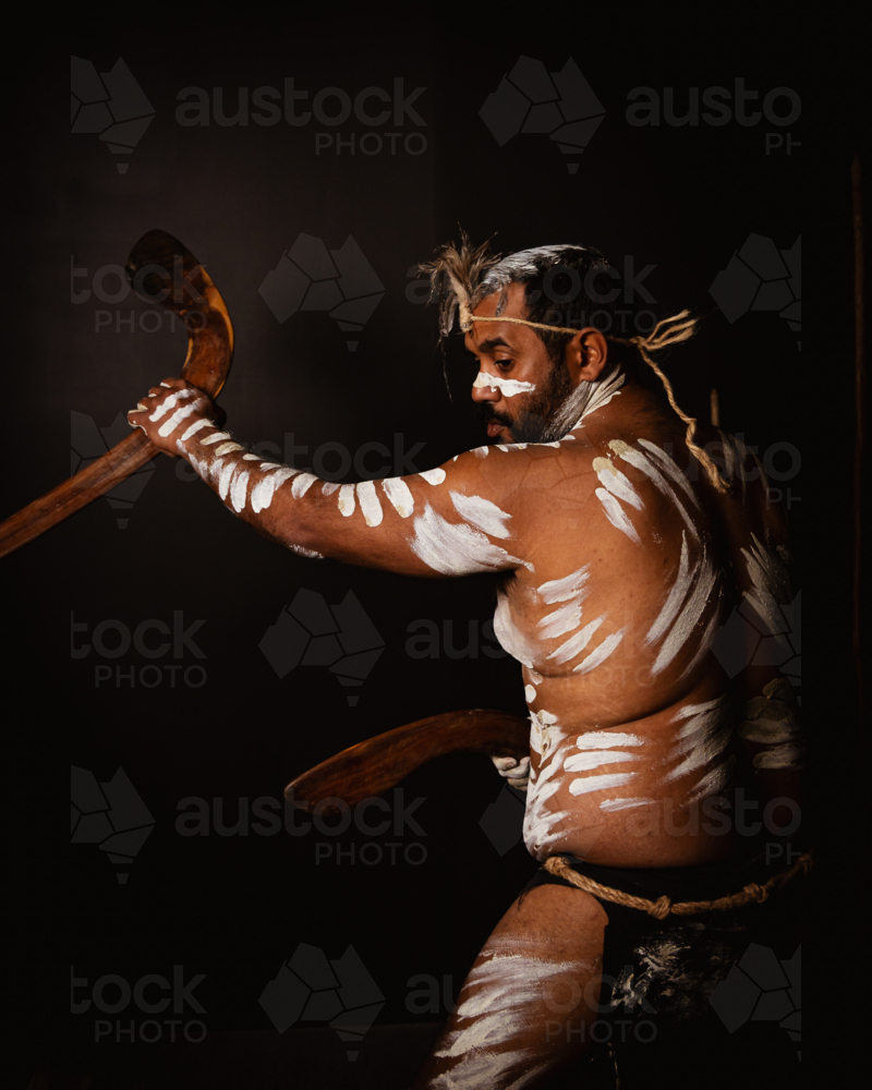 Aboriginal man holding a pair of boomerangs in a dark background. - Australian Stock Image