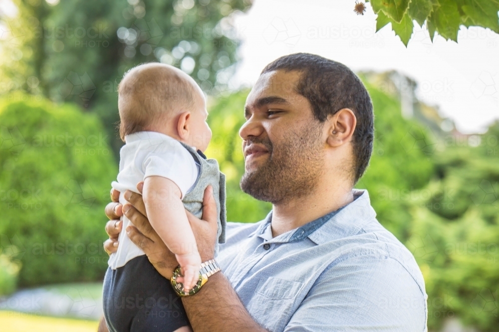 Aboriginal man holding baby up smiling - Australian Stock Image