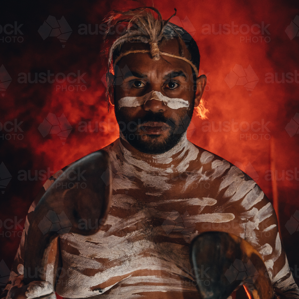 Aboriginal man holding boomerangs with red smokey background - Australian Stock Image