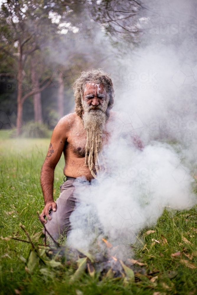 Aboriginal man kneeling in front of a fire - Australian Stock Image