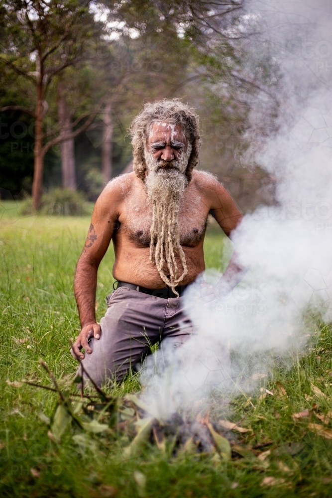 Aboriginal man kneeling next to a fire - Australian Stock Image