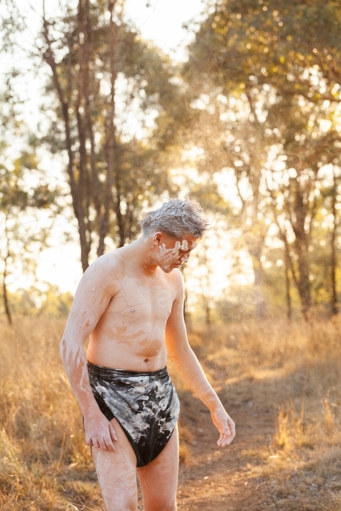 Aboriginal man standing in bushland at sunset in body paint and a lap lap - Australian Stock Image
