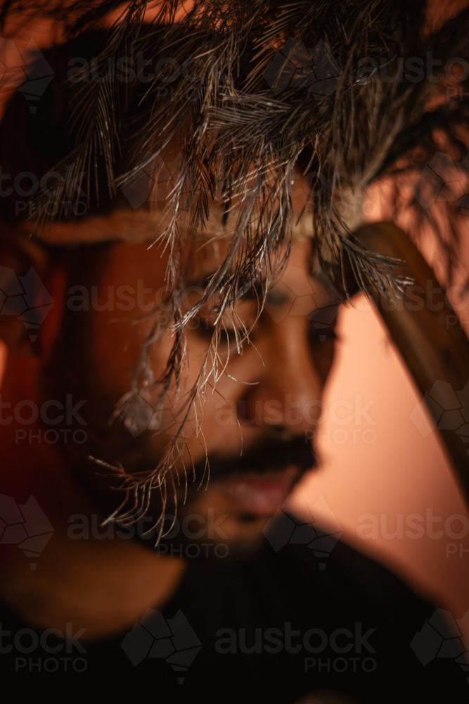 Aboriginal man wearing feathered headdress holding wooden boomerang close to his forehead - Australian Stock Image