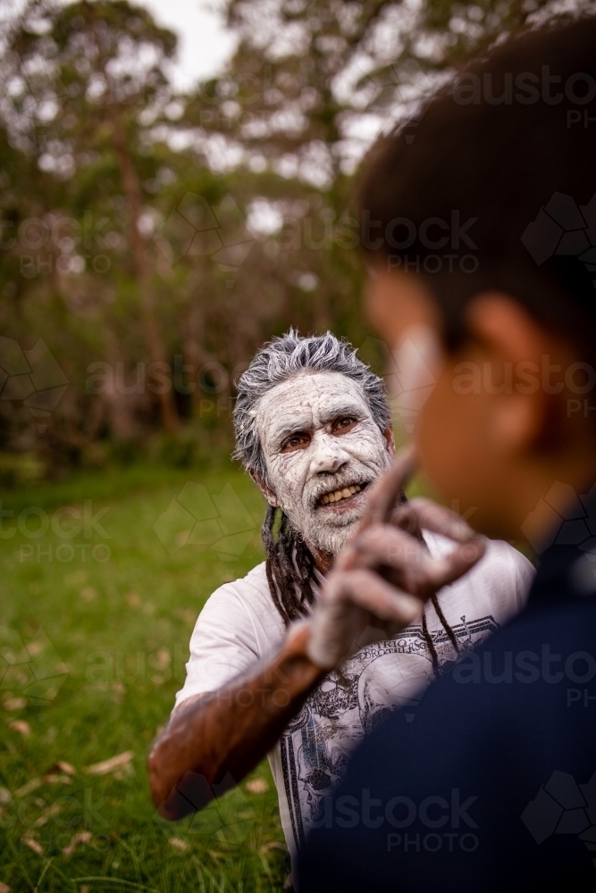 Aboriginal man wearing white face paint putting white face paint onto a young Aboriginal boy - Australian Stock Image