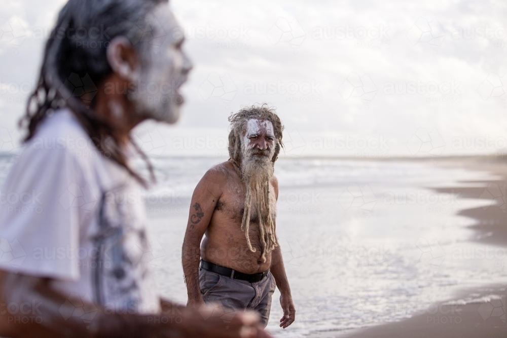 Aboriginal middle aged listening to another Aboriginal man talk on a beach - Australian Stock Image