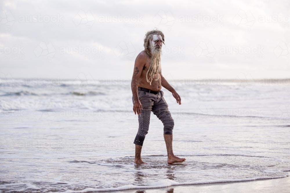Aboriginal middle aged man walking through water on a beach - Australian Stock Image