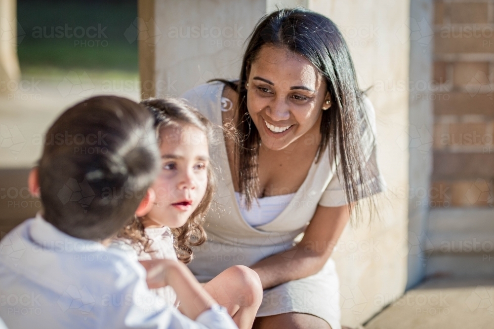 Aboriginal mother leaning forward laughing at twin children - Australian Stock Image