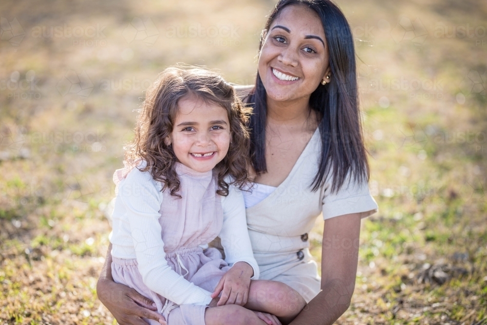 Aboriginal mother sitting on grass with mixed race daughter on lap - Australian Stock Image