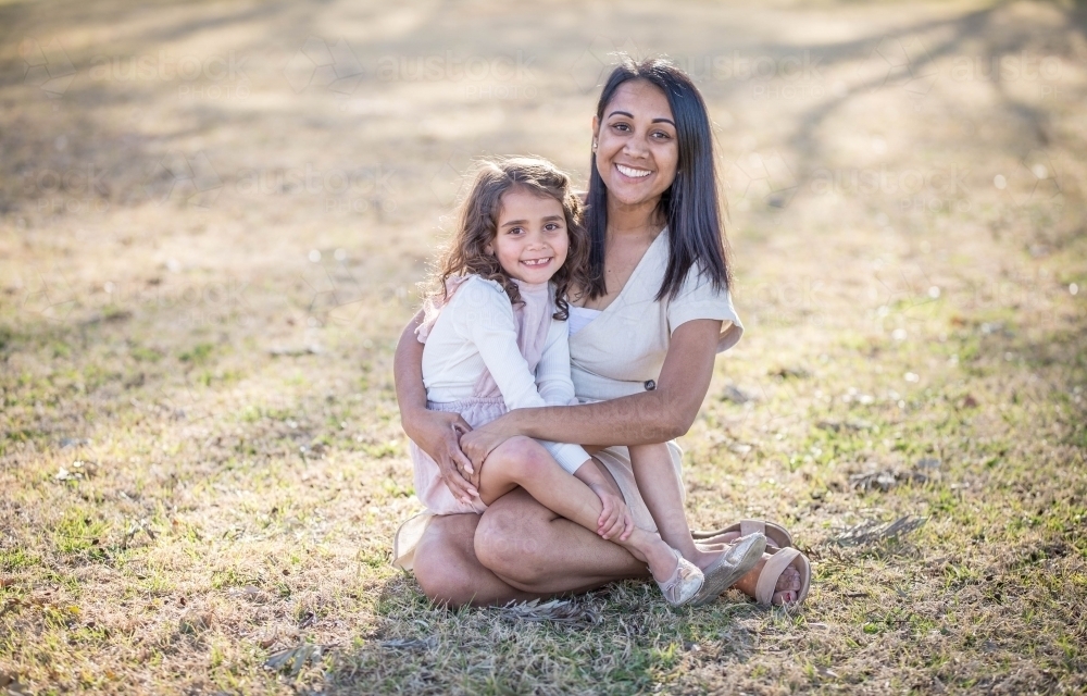 Aboriginal mother sitting with mixed race daughter on lap - Australian Stock Image