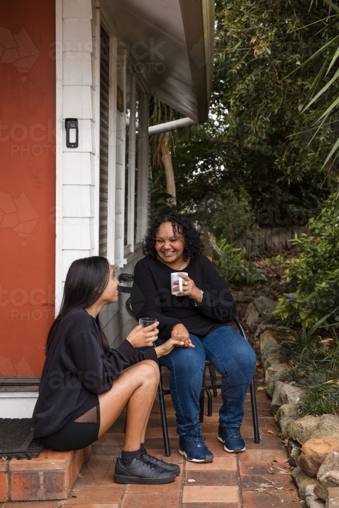 Aboriginal parent sitting together with teen on back porch - Australian Stock Image