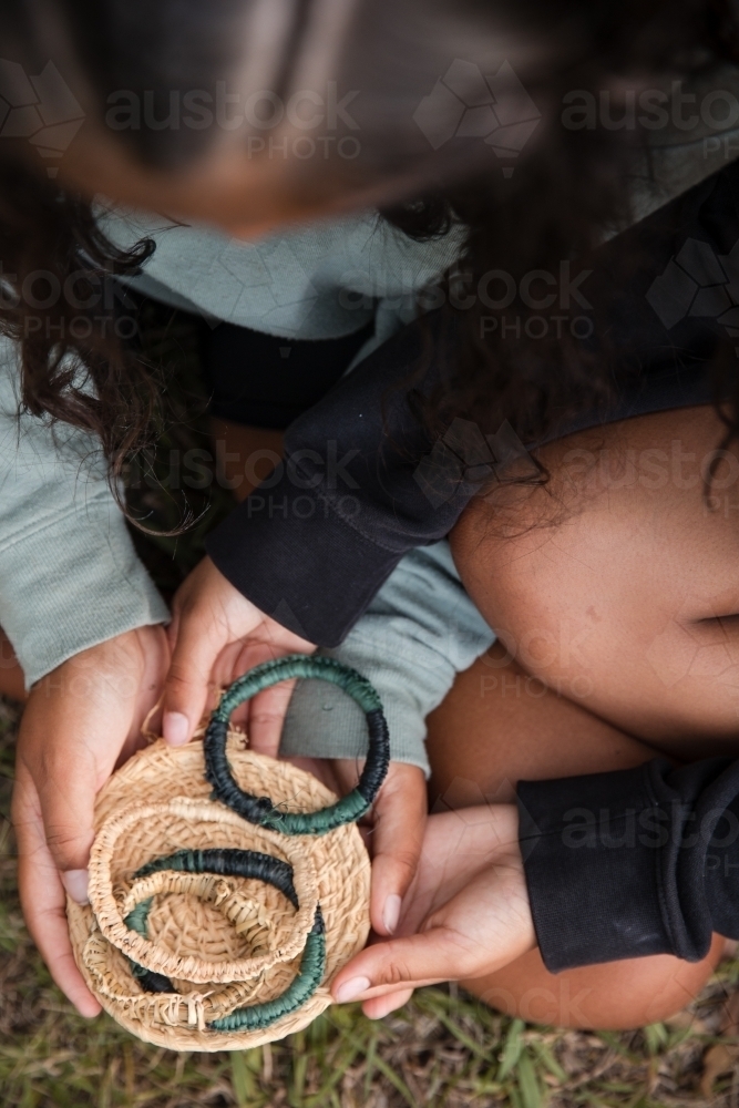 Aboriginal people sitting on grass, weaving baskets and bangles - Australian Stock Image