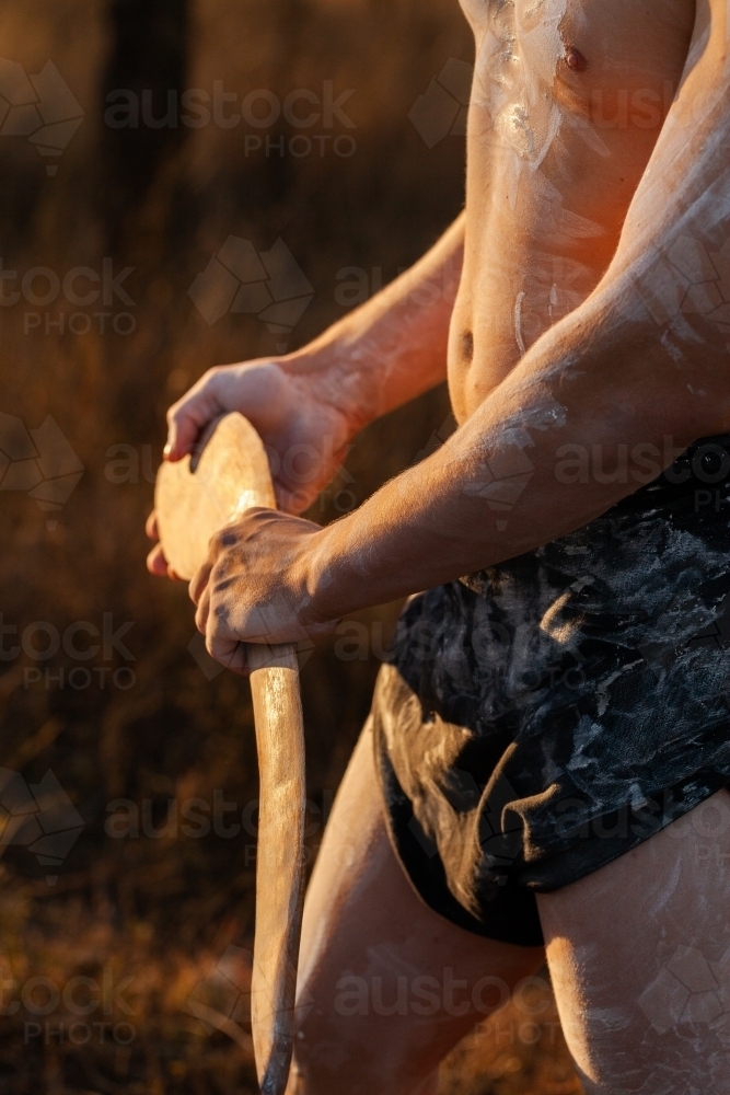 Aboriginal person dancing and telling cultural stories while holding digging and hunting stick - Australian Stock Image
