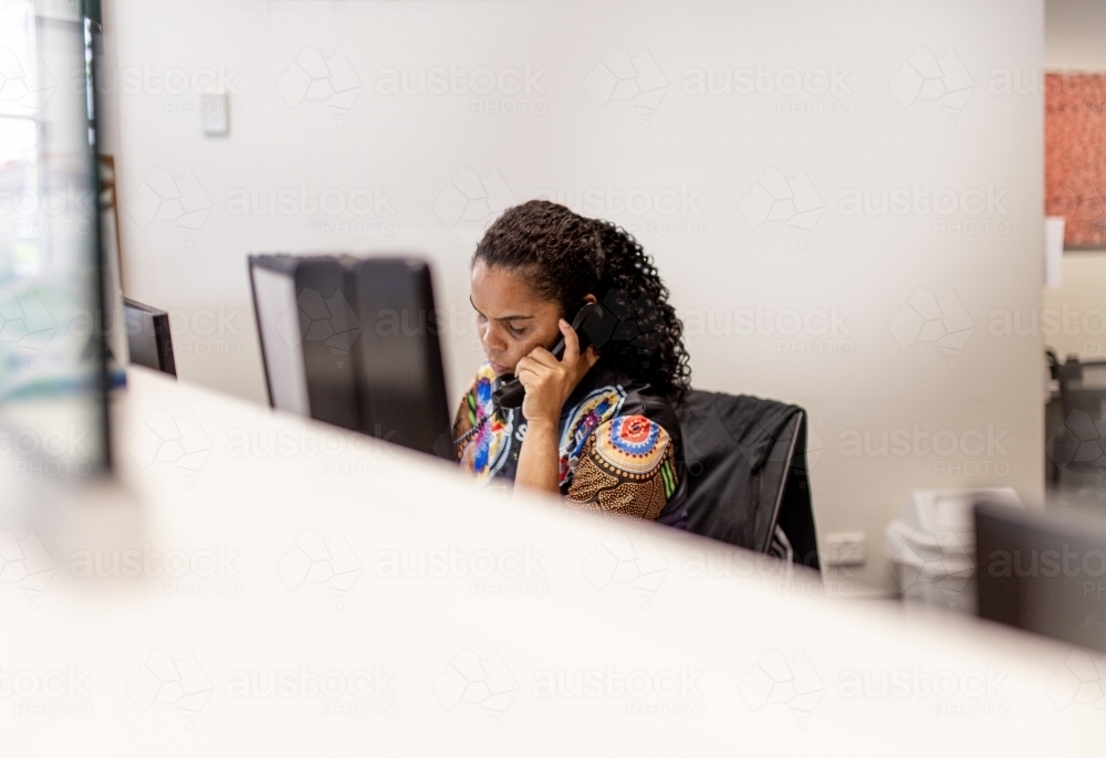 Aboriginal receptionist sitting talking on the phone - Australian Stock Image