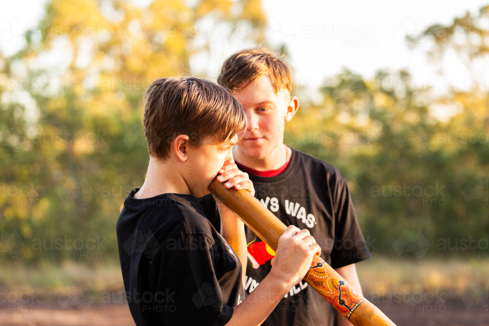 Aboriginal teen boys outside in rural Australia playing didgeridoo - Australian Stock Image