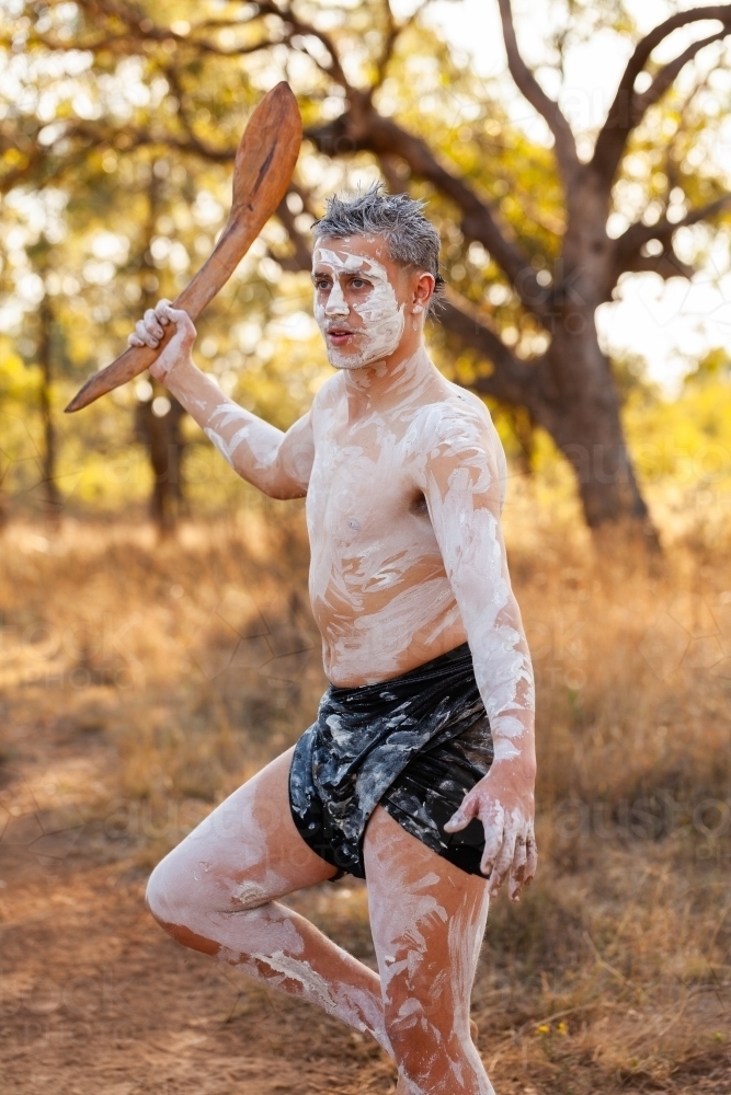 aboriginal teen holding club digging stick on country with bokeh bushland background - Australian Stock Image