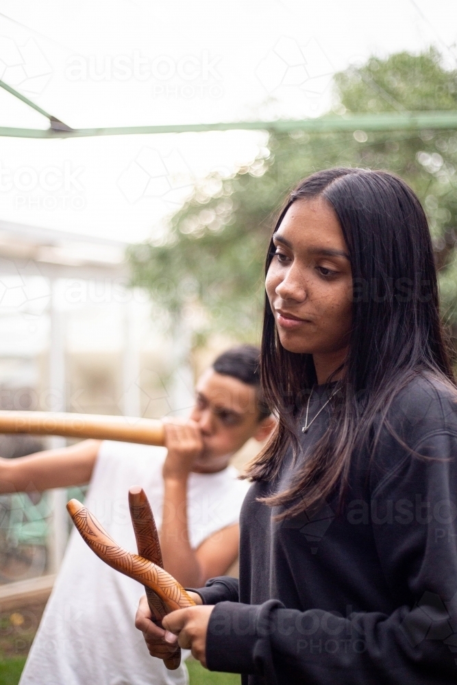 Aboriginal teenage girl with musical sticks in her backyard  with her brother - Australian Stock Image