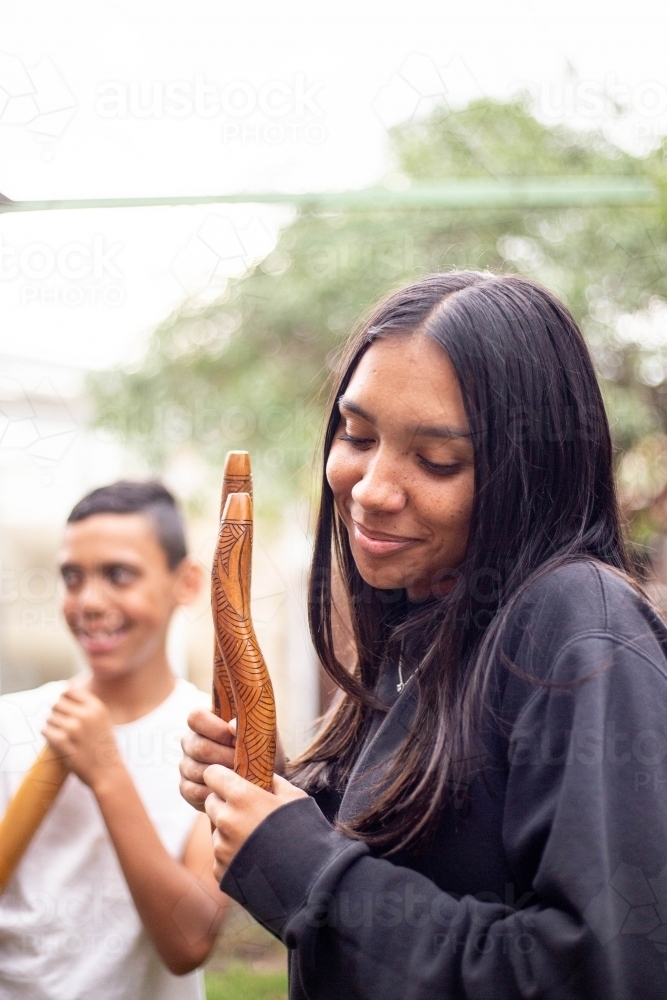 Aboriginal teenage girl with musical sticks in her backyard  with her brother - Australian Stock Image
