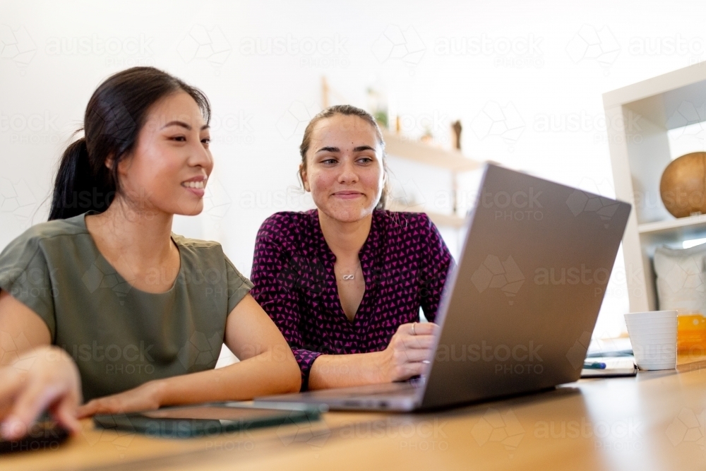 Aboriginal woman and Asian woman sitting together in an office looking at a laptop screen - Australian Stock Image