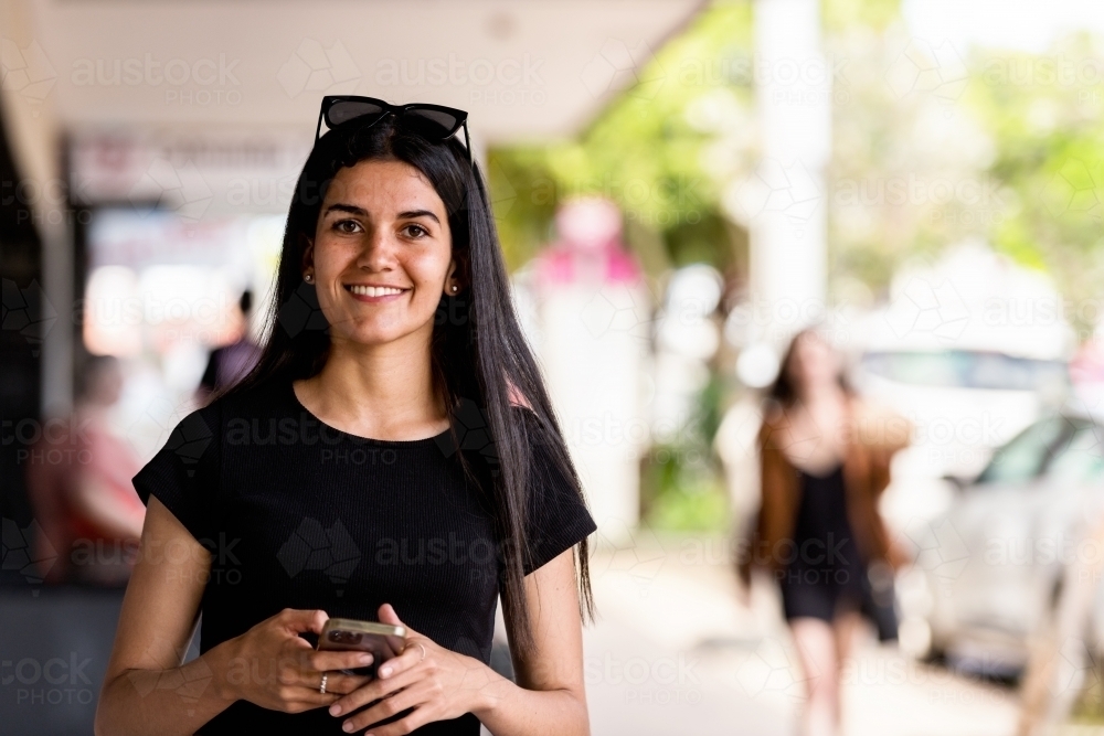 aboriginal woman walking in an urban setting, using mobile phone - Australian Stock Image