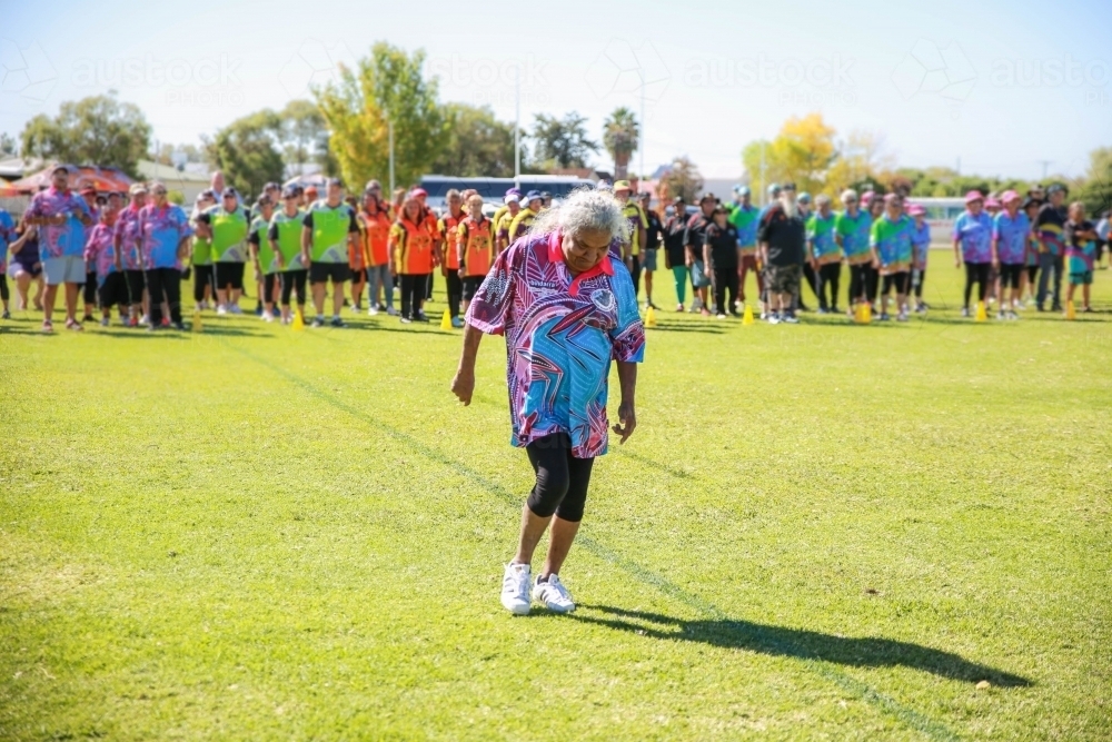 Aboriginal woman walking relay while teams watch - Australian Stock Image