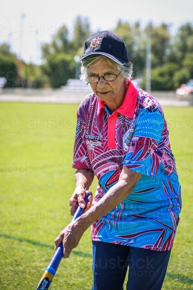 Aboriginal woman wearing hat and glasses holding hockey stick - Australian Stock Image