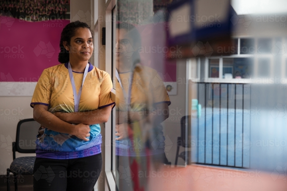 Aboriginal woman wearing lanyard looking out window - Australian Stock Image