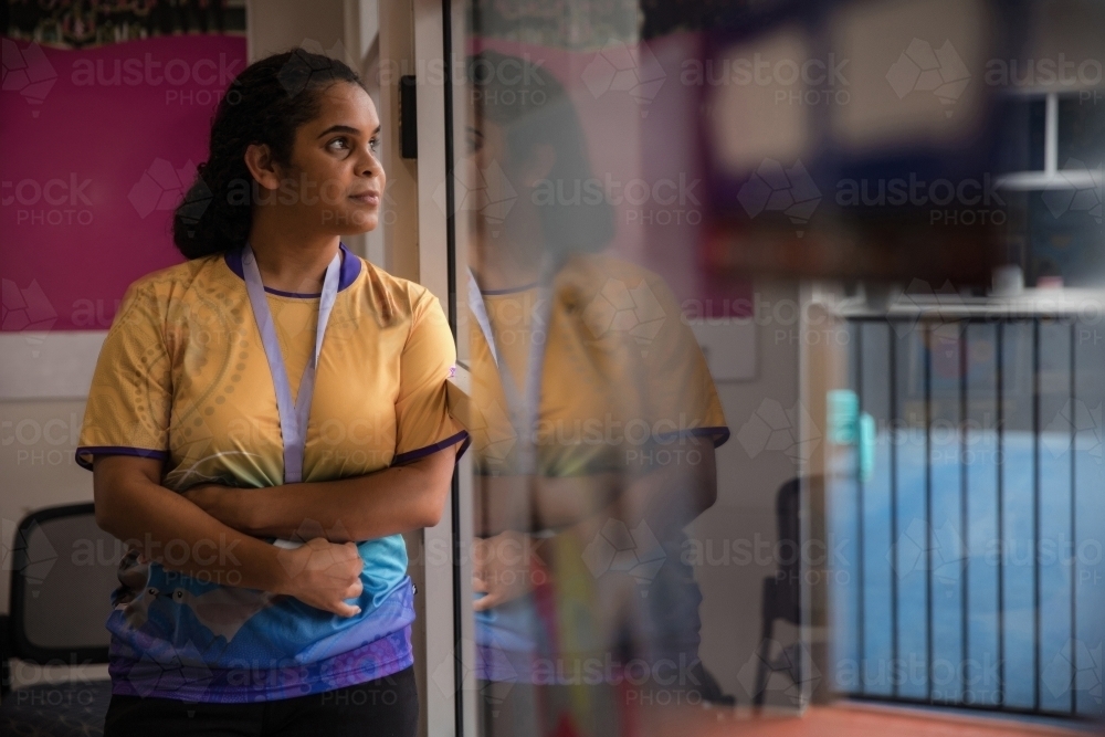 Aboriginal woman wearing lanyard looking out window - Australian Stock Image