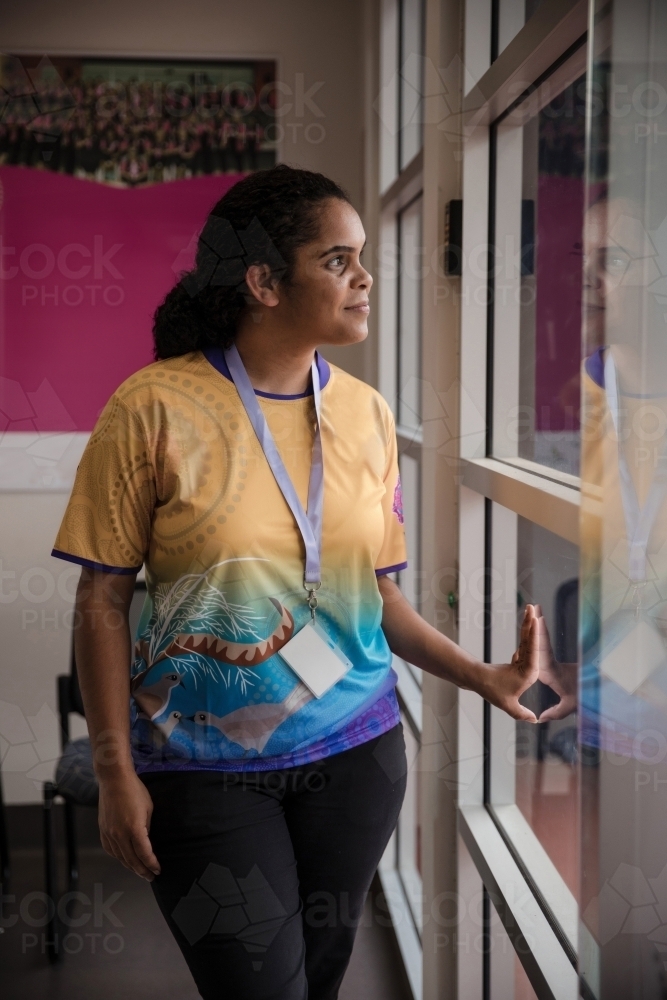 Aboriginal woman wearing lanyard looking out window - Australian Stock Image