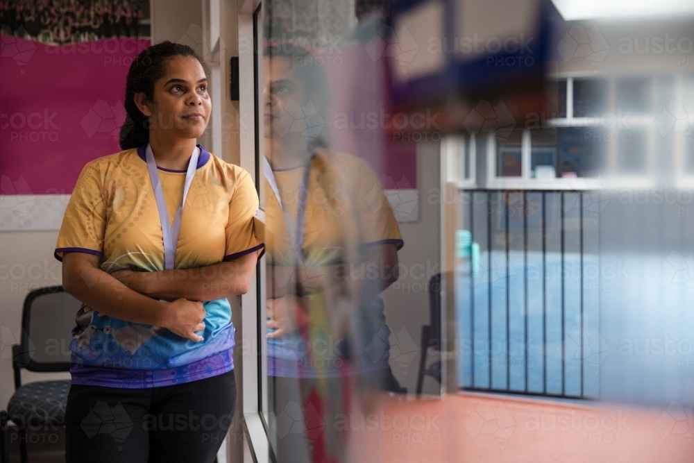 Aboriginal woman wearing lanyard looking out window - Australian Stock Image