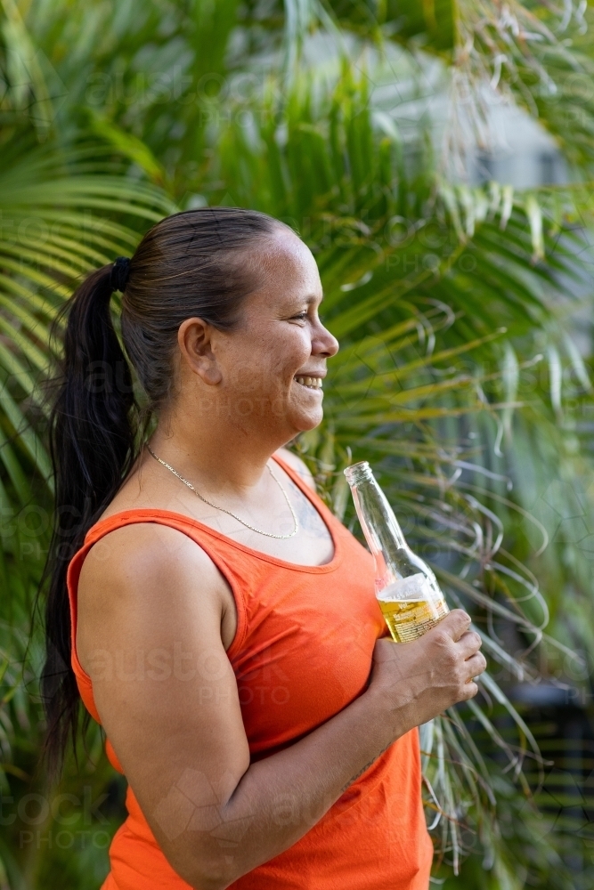 aboriginal woman with long hair in profile holding a bottle of beer - Australian Stock Image