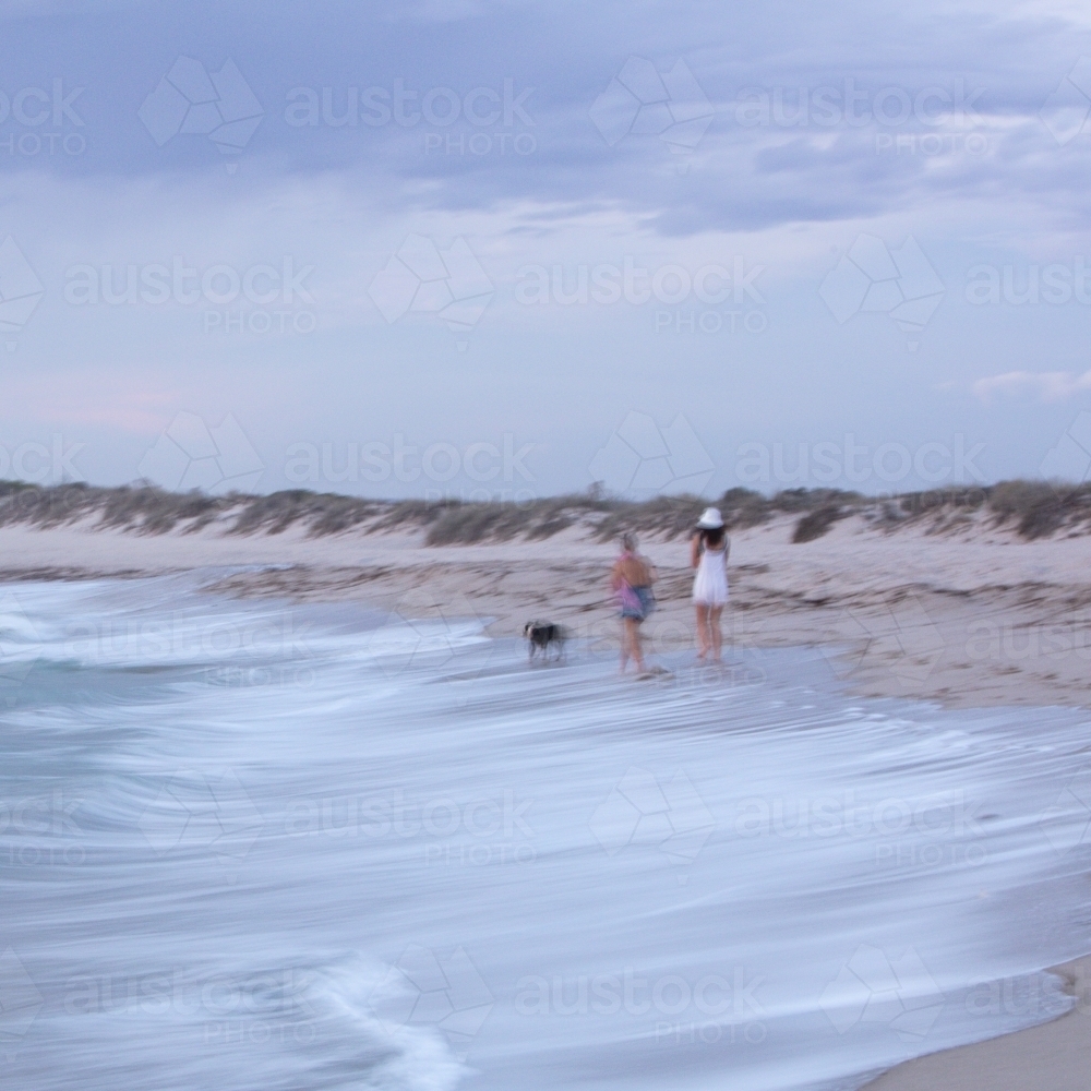 Abstract image of two people walking the dog at the beach - Australian Stock Image